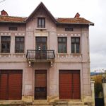 Two-storey representative house with symmetrical facade, central balcony, wrought iron railing, decorative consoles, mascarons and vegetal motifs.